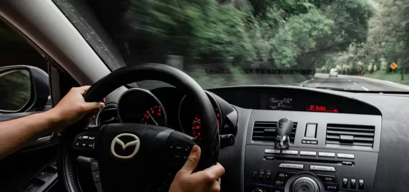 Vista interior del tablero de un coche Mazda con las manos del conductor en el volante.